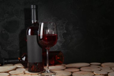 Siyah grunge arka planına karşı ahşap masada şişe ve bir bardak kırmızı şarap.