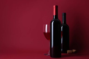 Kırmızı arka planda şişeler, bir bardak şarap ve mantar.