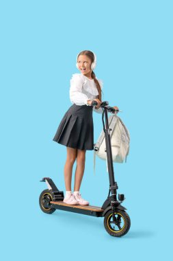 Mavi arka planda elektrikli scooter kullanan kulaklıklı tatlı bir kız öğrenci.