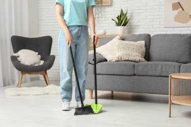 Kadın oturma odasında süpürge ve faraşla yerleri süpürüyor.