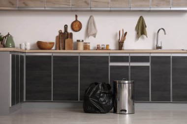 Mutfakta yerde çöp torbası dolu bir çöp kutusu.