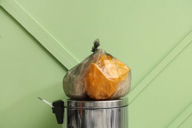 Yeşil duvarın yanında çöp kutusu ve çöp torbası var.