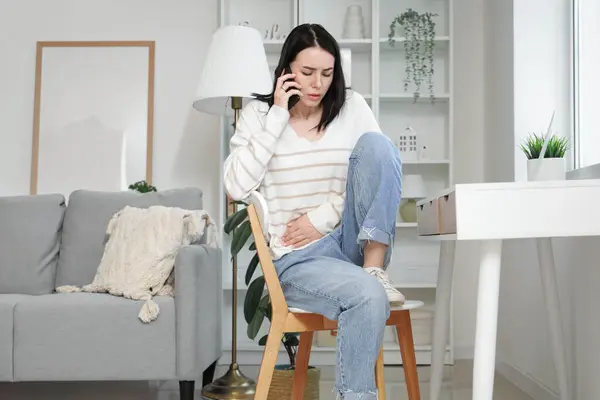 stock image Young woman with severe abdominal pain calling an ambulance at home