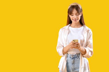 Sarı arka planda cep telefonu kullanan güzel genç bir kadın.