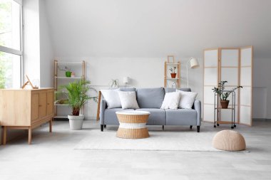 Gri kanepe, masa ve raf üniteleriyle aydınlık oturma odasının içinde.