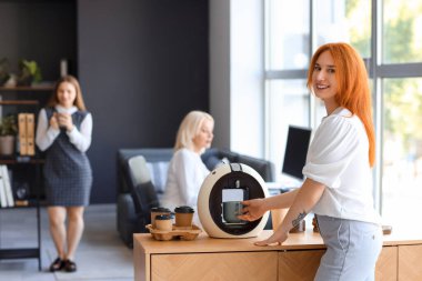 Genç bayan ofiste kahve yapıyor.