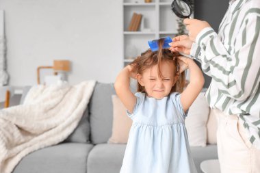 Anne elinde büyüteçle küçük kızının saçını pedikülozla tarıyor.