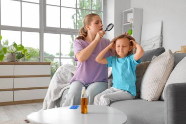 Mother with magnifier checking her little daughter's head with pediculosis at home clipart