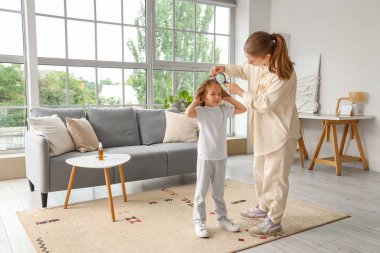 Anne elinde büyüteçle küçük kızının saçını pedikülozla kontrol ediyor.