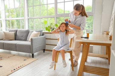 Mother combing her little daughter's hair with pediculosis at home clipart