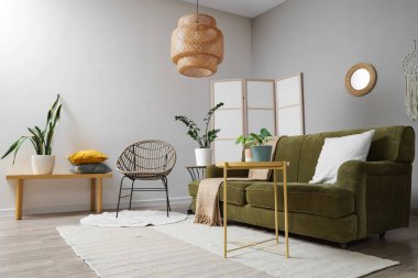 Ayna, yeşil kanepe ve koltuklu aydınlık oturma odasının içi.