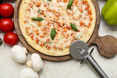 Lezzetli pizza, kesici ve arka planda bulunan malzemeler.