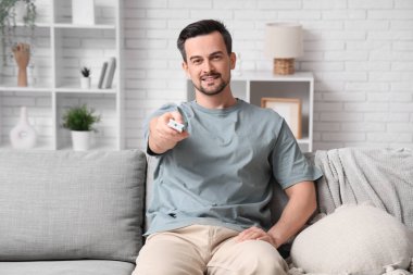 Yakışıklı delikanlı kanepede oturuyor ve oturma odasındaki klimayı açıyor.