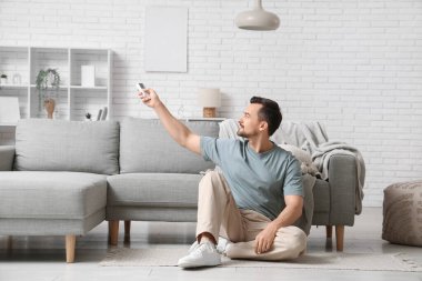 Klimalı uzaktan kumandalı genç adam beyaz tuğla duvarın yanında yerde oturuyor.