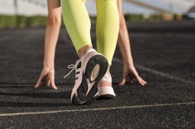Çömelmiş spor yapan genç bir kadın stadyumda başlangıç pozisyonu, arka görüş