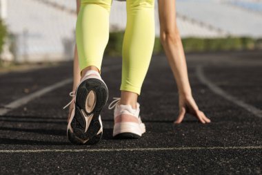 Çömelmiş spor yapan genç bir kadın stadyumda başlangıç pozisyonu, arka görüş