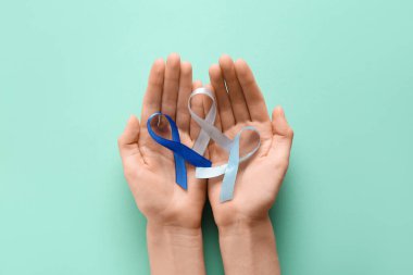 Turkuaz arka planda renkli kurdeleli bir kadın eli. Dünya Kanser Günü