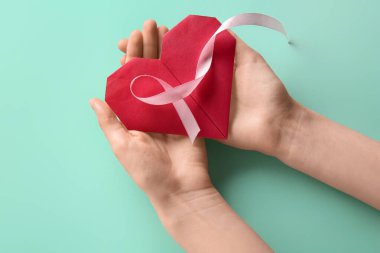 Pembe kurdeleli ve turkuaz arka planda kalbi olan kadın eller. Dünya Kanser Günü
