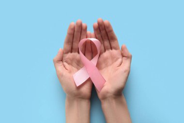Mavi arka planda pembe kurdeleli kadın eller. Dünya Kanser Günü