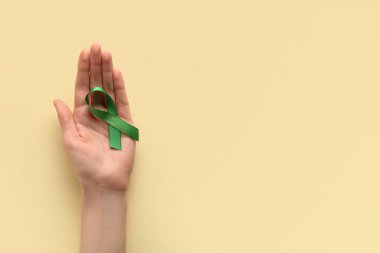 Sarı arka planda yeşil kurdeleli bir kadın. Dünya Kanser Günü