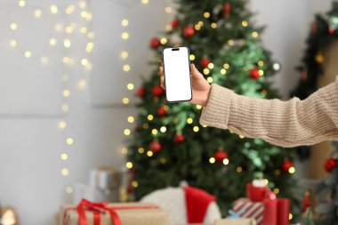 Evde parlayan Noel ağacına karşı cep telefonu olan bir kadın.