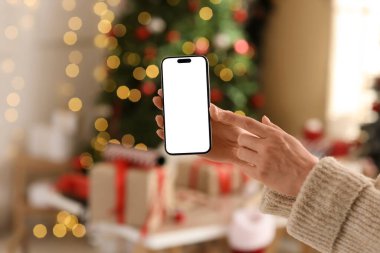 Odada parlayan Noel ağacının yanındaki cep telefonuna bakan kadın elleri