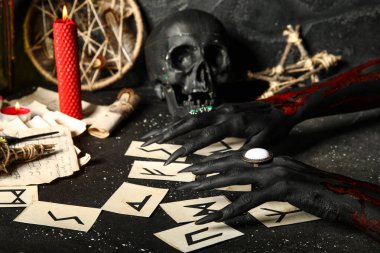 Yaşlı Futhark mühür kartlarıyla kanlı cadı elleri ve grunge siyah arka planda sihirli özellikler. Cadılar Bayramı