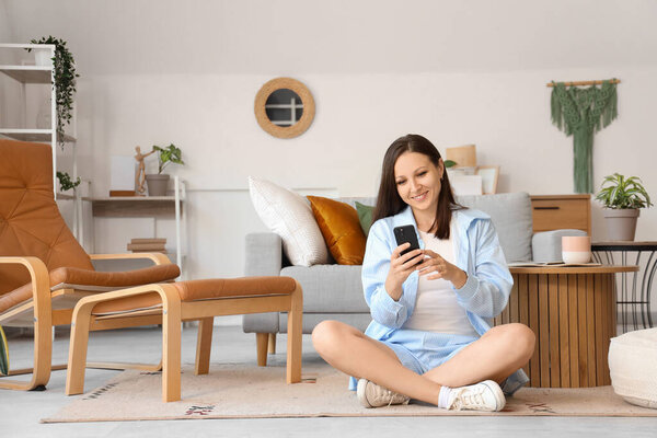 Young woman using mobile phone on carpet at home
