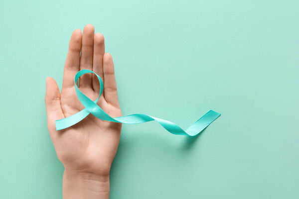 Женская рука со светло-голубой лентой на бирюзовом фоне. Всемирный день борьбы против рака
