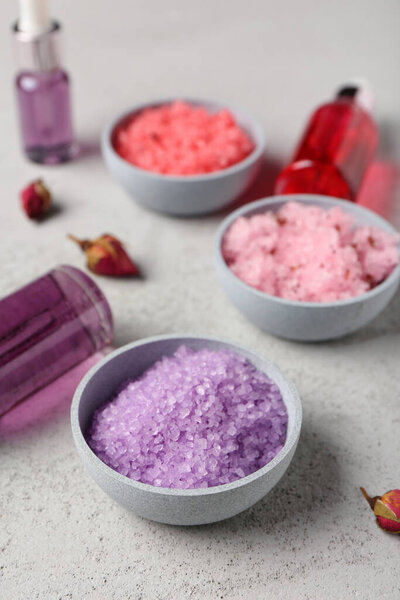 Чаши с натуральными скрабами для тела, бутылки эфирного масла и бутоны роз на светлом фоне