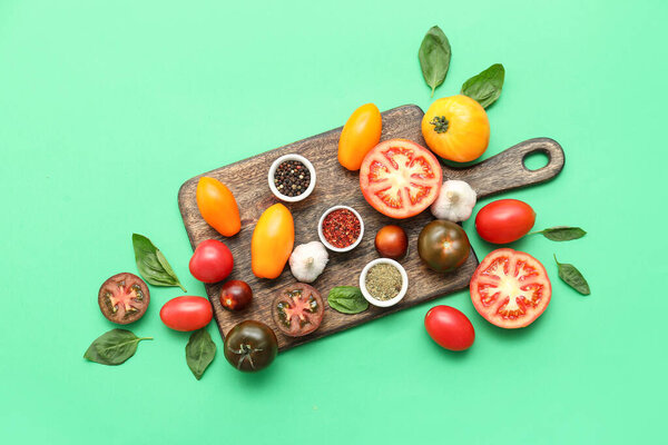 Wooden board with fresh ripe tomatoes and different spices on green background