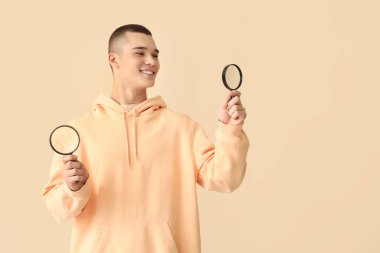 Young man with magnifiers on beige background clipart