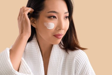 Yüzünde bej rengi krem olan güzel bir Asyalı kadın.