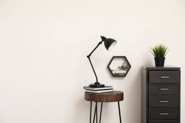 Masa lambası küçük masada ve dosya dolabı beyaz duvarın yanında.