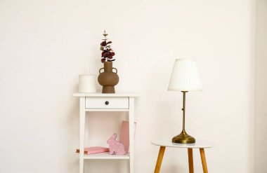 Tuvalet masasında okaliptüs dalları ve beyaz duvarın yanında lamba olan vazo.