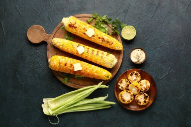 Tahta tahta ve koyu arkaplanda tereyağlı bir tabak lezzetli ızgara mısır koçanı.