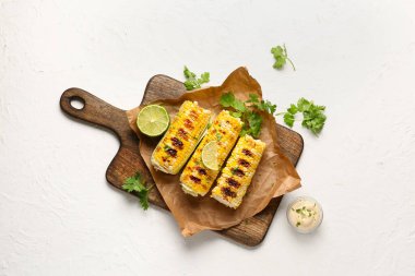 Lezzetli ızgara mısır koçanı ve beyaz arka planda limon içeren fırın kağıdı.