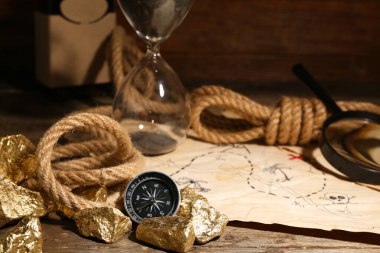 Hazine haritalı seyahat ekipmanları ve kahverengi ahşap arka planda altın külçeler.