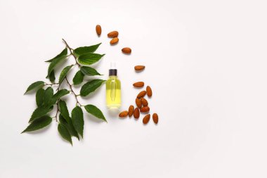 Bademli bir şişe kozmetik yağı ve beyaz arka planda yapraklar.