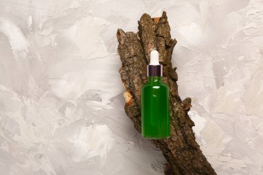 Gri arka planda ağaç kabuğu olan bir şişe kozmetik yağı.