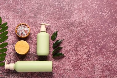 Bottles and jar of cosmetic products with sea salt on purple background