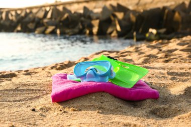 Yeni yüzme maskesi, yüzgeçler ve deniz kenarındaki kumda havlu.