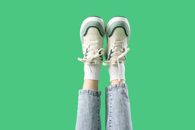 Yeşil arka planda şık ayakkabılar giyen genç kadınların bacakları.