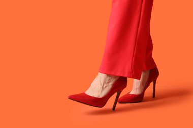 Turuncu arka planda kırmızı topuklu genç bayanın bacakları.