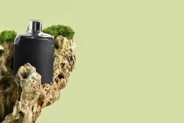 Yeşil arka planda siyah parfüm şişesi ve ağaç kabuğu.