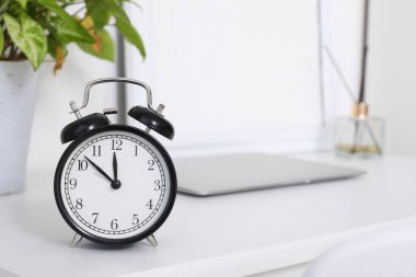 Alarm saati, dizüstü bilgisayarı ve ev bitkisi olan beyaz masa, yakın plan.
