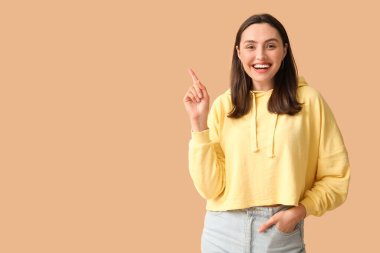 Kahverengi arka planda bir şeye işaret eden gülümseyen genç kadın.