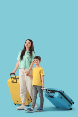 Anne ve bavulları mavi arka planda yürüyen küçük oğlu.