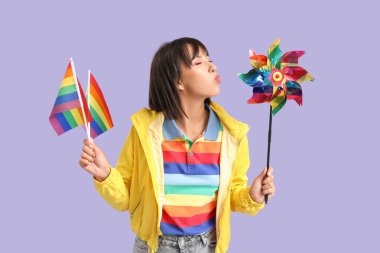 LGBT bayrakları ve eflatun arka planda renkli oyuncak yel değirmeni olan güzel genç bir kadın.