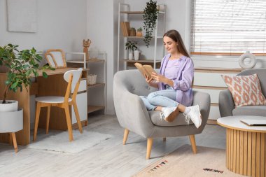 Genç ve güzel bir kadın evdeki koltukta kitap okuyor.